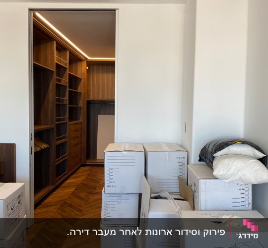 קופסאות קרטון מסודרות ליד ארון עץ פתוח